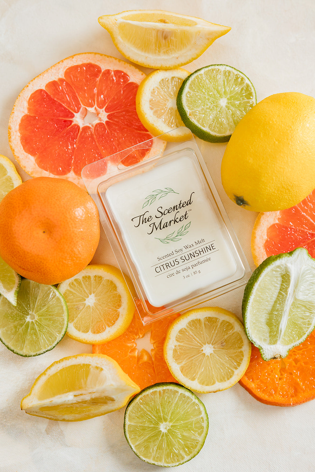 Scented candle labeled 'Citrus Sunshine' surrounded by citrus fruits on a light background