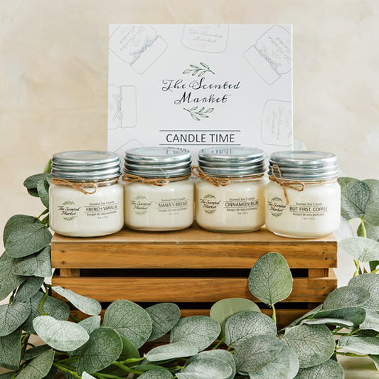 Four candles in jars with metal lids on a wooden stand, surrounded by eucalyptus leaves, with 'The Scented Market' branding.