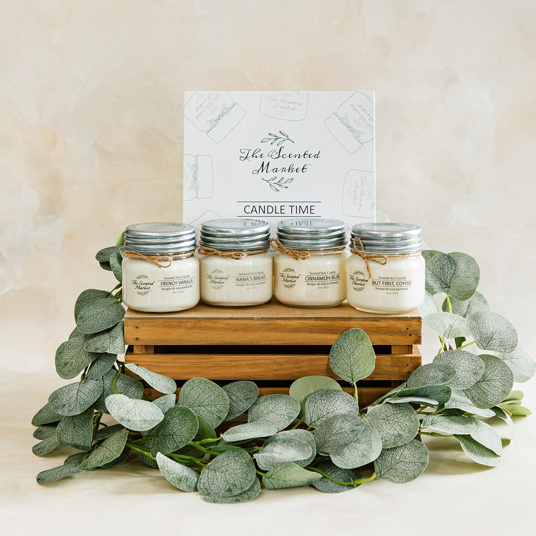 Set of candles in jars on a wooden crate with eucalyptus leaves against a beige background
