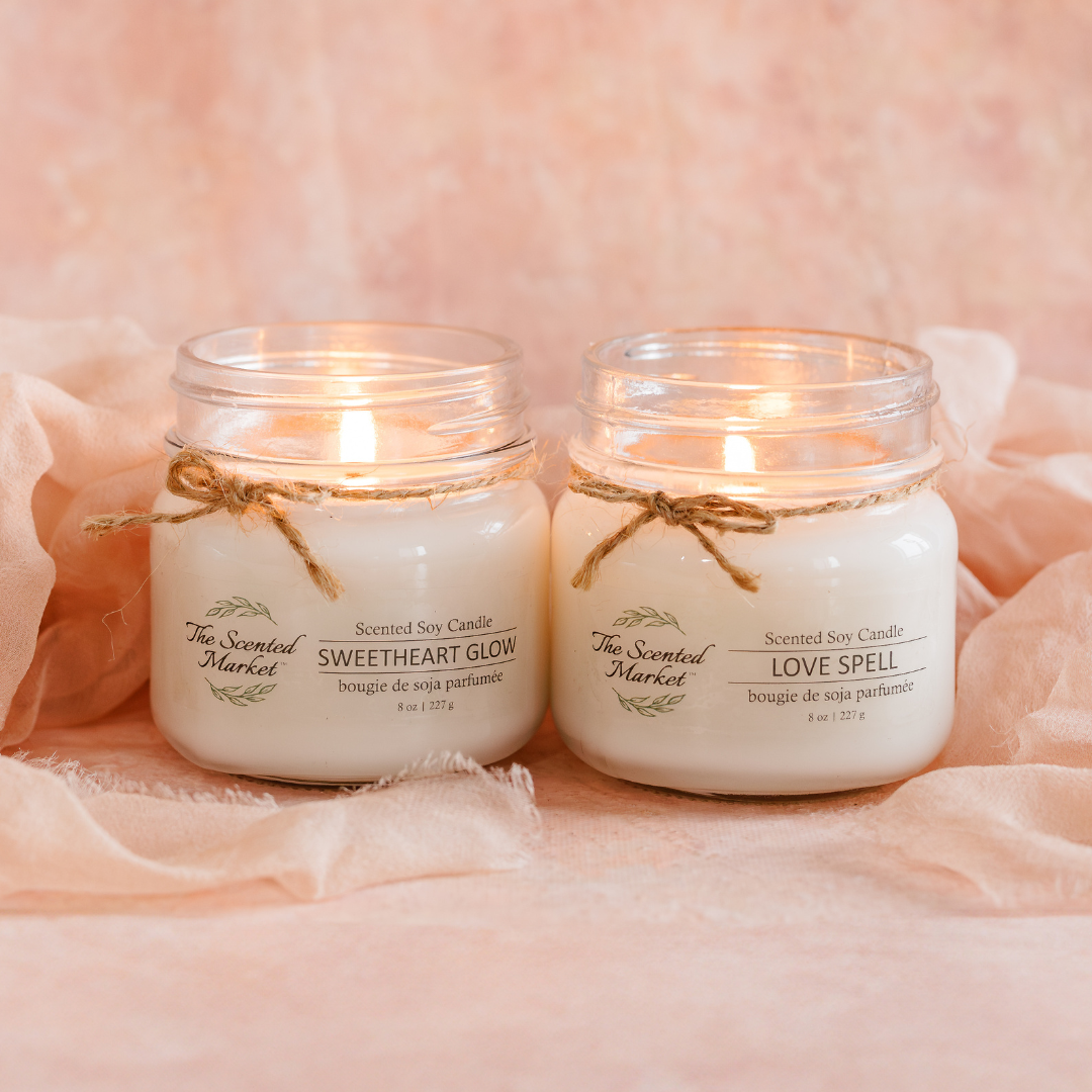 Two lit candles in glass jars with labels on a soft pink background