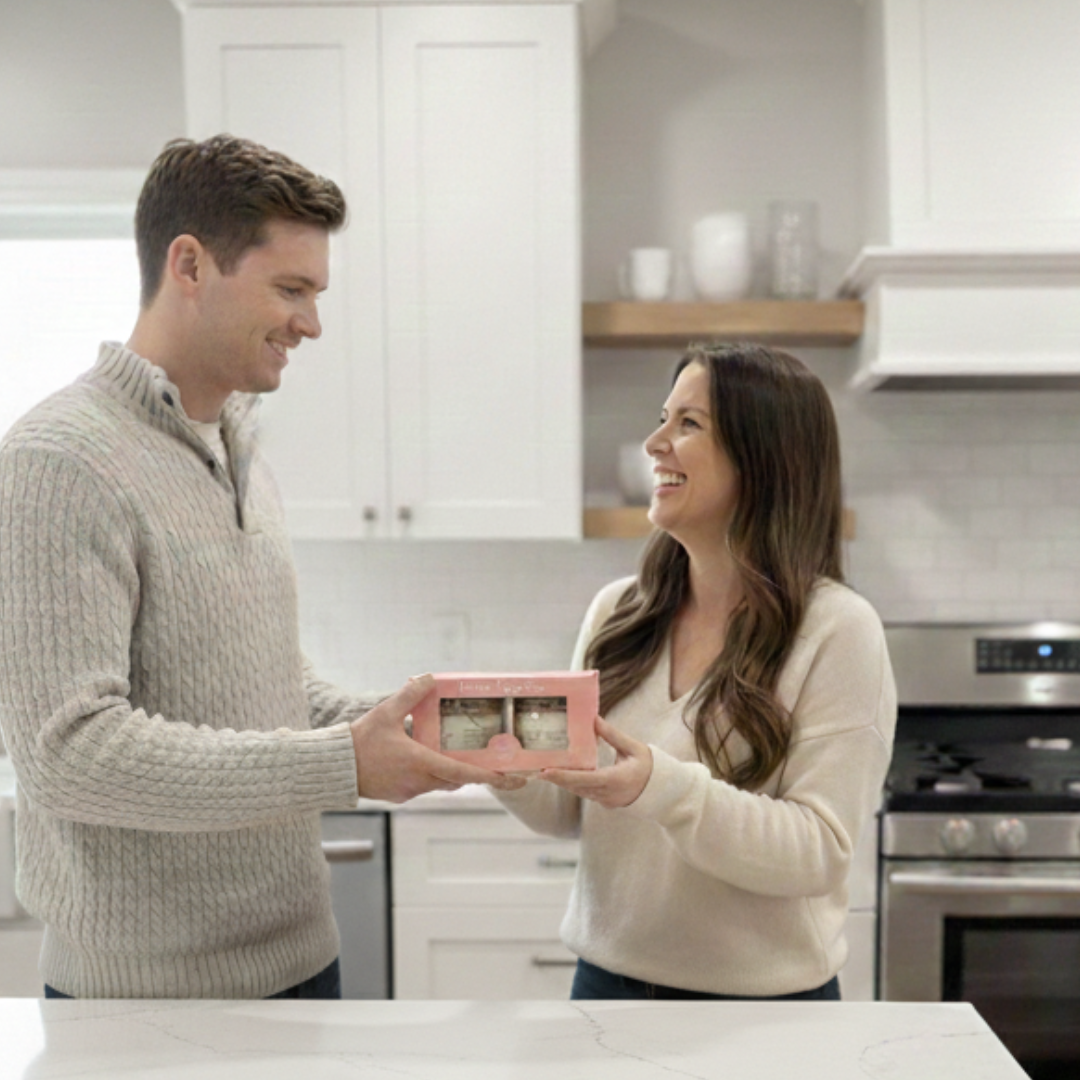 Man and woman in a kitchen holding a pink box with small items.