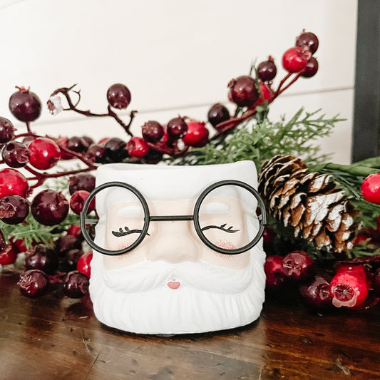 Decorative Santa Claus candle holder with glasses on a wooden surface with Christmas decorations.