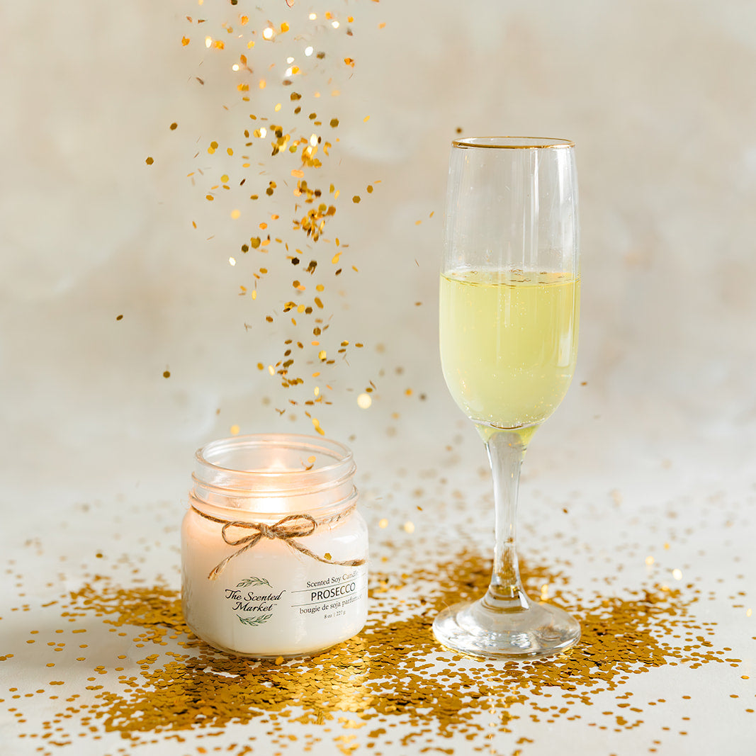 Glass of champagne and candle with gold confetti on a light background