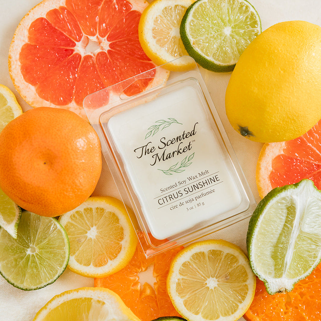 Scented candle labeled 'Citrus Sunshine' surrounded by citrus fruits on a light background