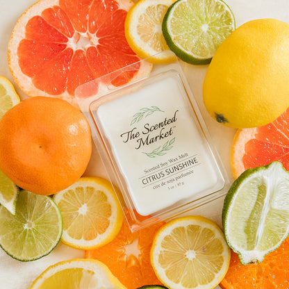 Scented candle labeled 'Citrus Sunshine' surrounded by citrus fruits on a light background