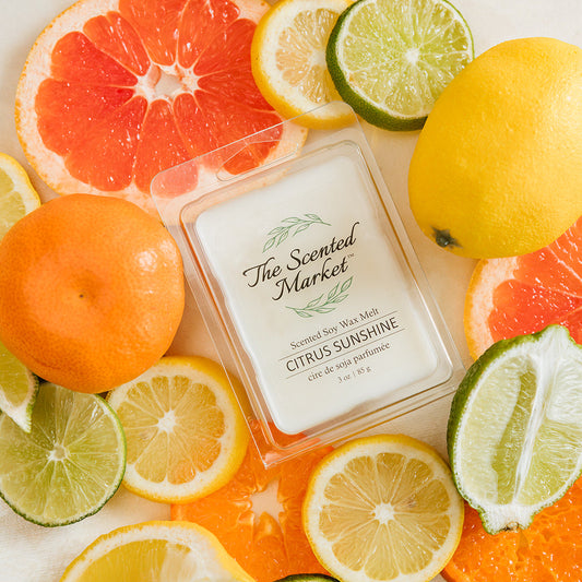 Scented candle labeled 'Citrus Sunshine' surrounded by citrus fruits on a light background