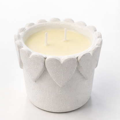 Candle in a textured white holder with heart designs on a white background