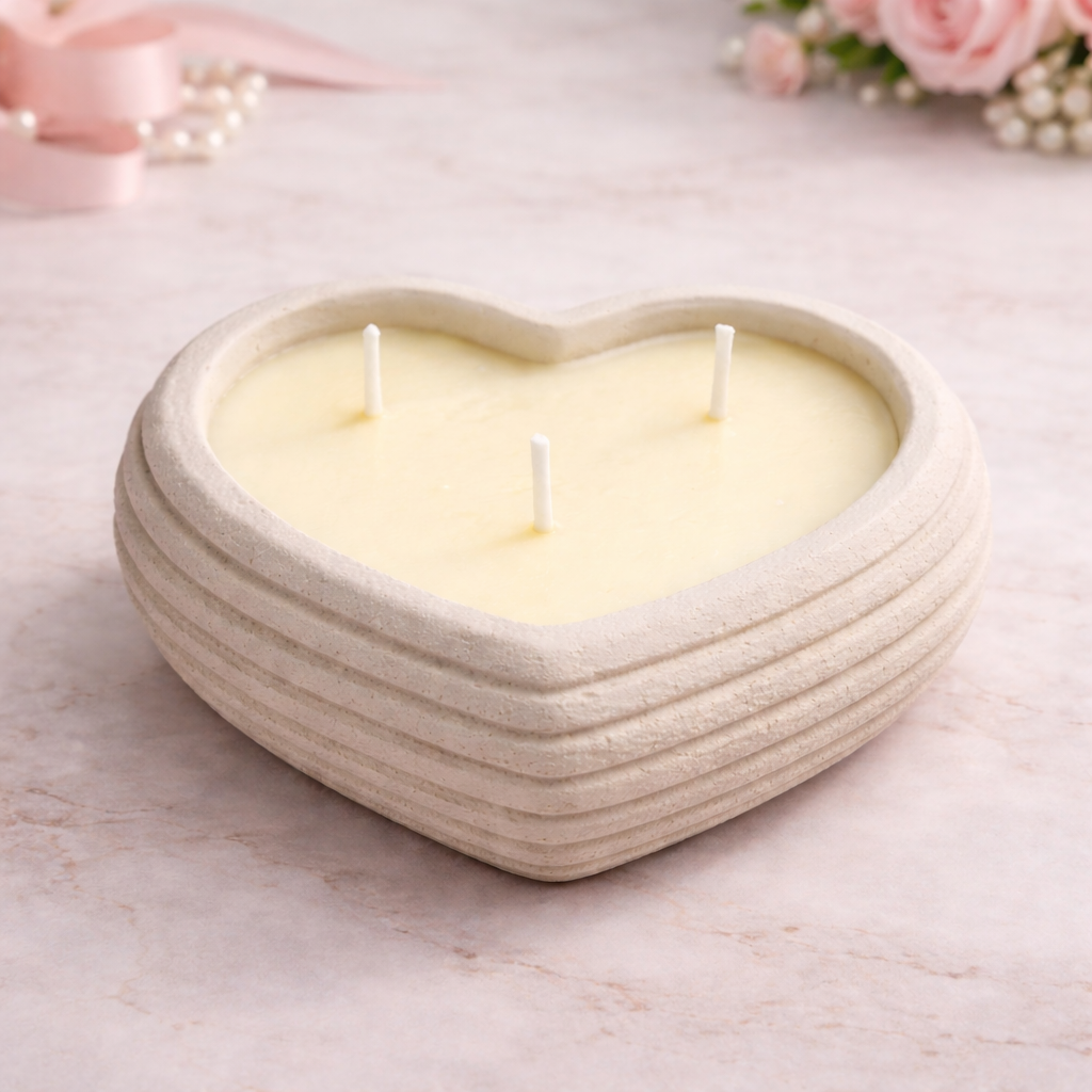 Heart-shaped candle in a ceramic holder on a light surface with flowers in the background