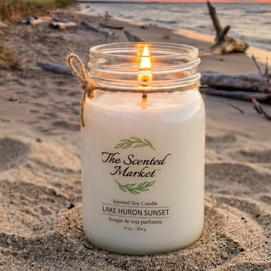 Candle in a jar labeled 'The Scented Market' on a beach at sunset.
