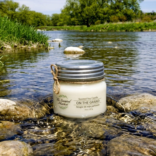 Mason jar candle labelled 'On The Grand' sitting in the rocky waters of the Grand River, Ontario with greenery in the background