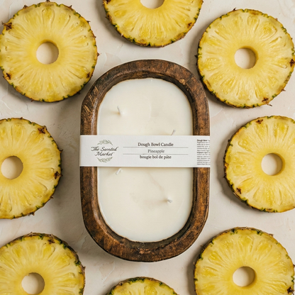 Candle in a wooden container surrounded by pineapple slices on a light background