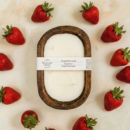 White candle in a wooden holder surrounded by strawberries on a light background