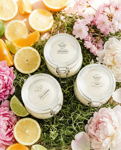 Three white jars with labels on a bed of green moss and flowers, surrounded by sliced lemons and oranges.